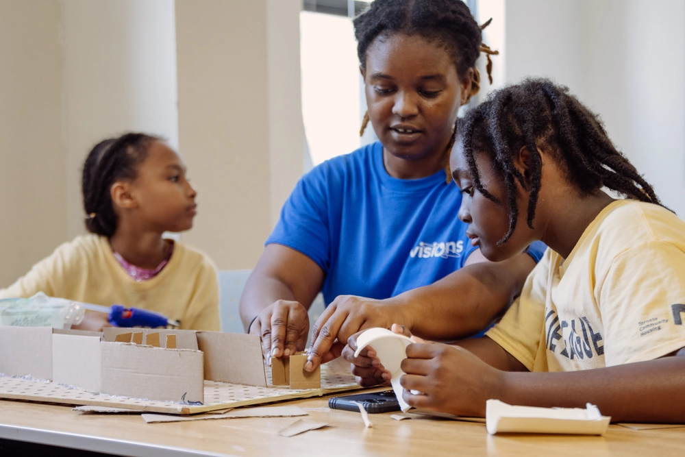 An adult and two children work together on a craft project at a table with cardboard and paper.