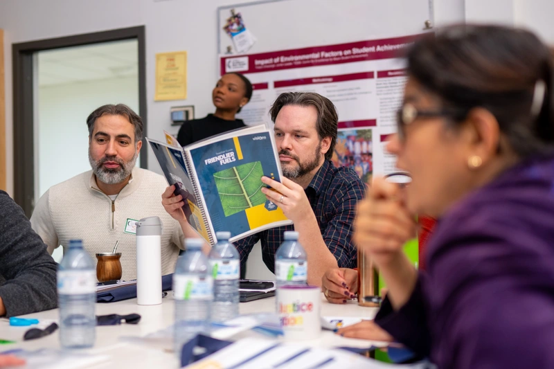 People sit around a table with water bottles; one man reads a Principles Fuel booklet.
