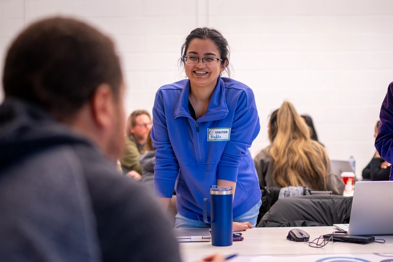Woman in blue jacket smiles while talking to others at a table in a casual meeting setting.