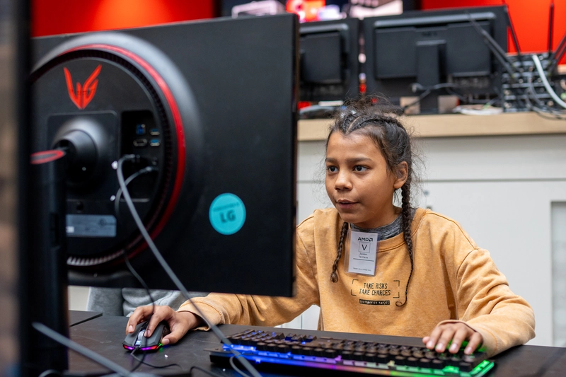 Young person focused on playing a computer game at a gaming setup with keyboard and monitor.