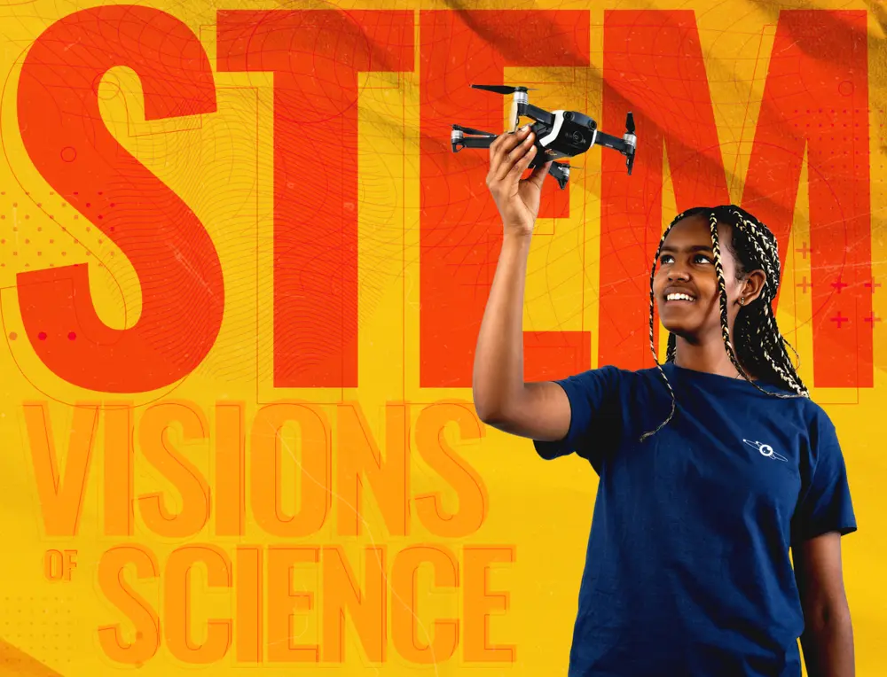 Smiling person holds a drone, standing in front of the words STEM Visions of Science on a bright background.