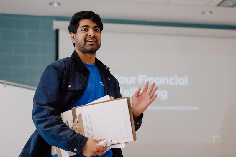 Man holding clipboards and speaking in front of a projected financial workshop presentation.