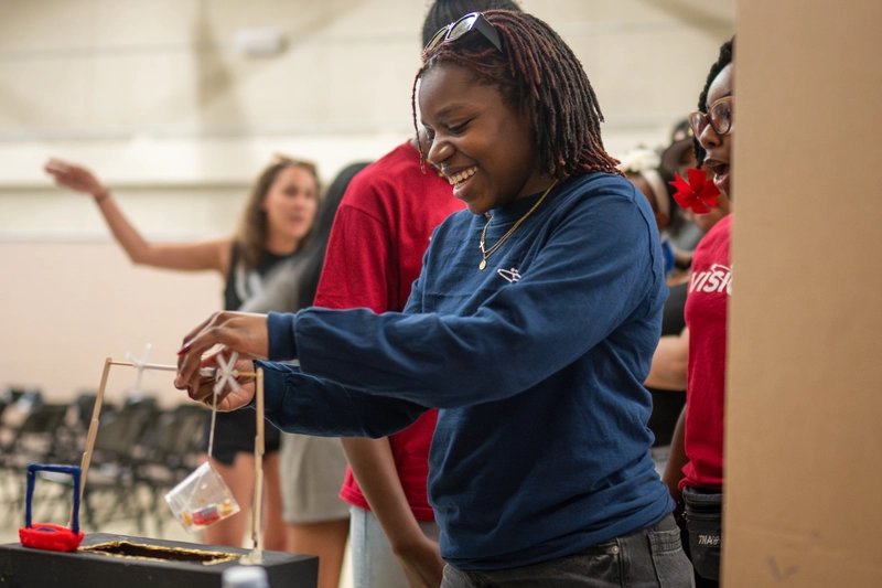 Smiling young woman participates in a classroom activity with others in the background.