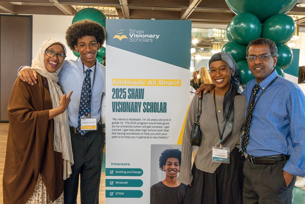 Four people stand smiling next to a Shaw Visionary Scholars sign with balloons in the background.
