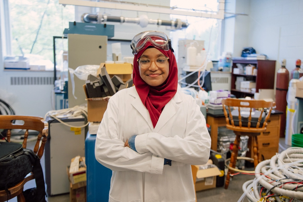 A scientist in a lab coat and goggles stands confidently in a busy laboratory.