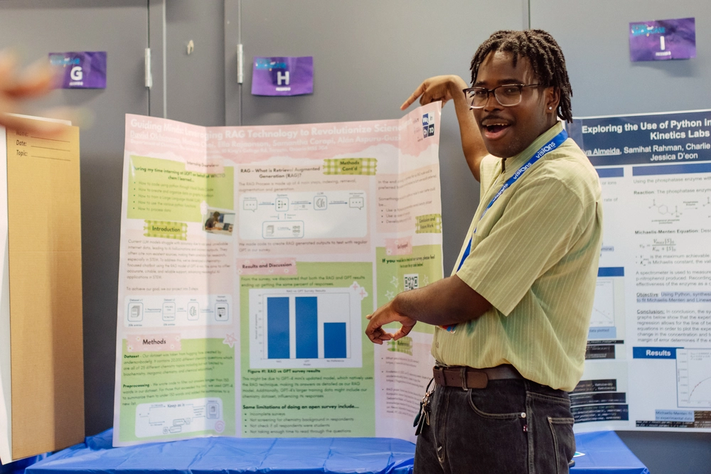 A person with glasses points enthusiastically to a science fair project display with charts and diagrams.