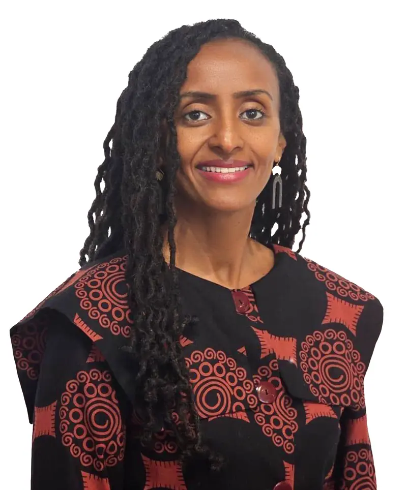 Woman with long braided hair, wearing a patterned black and red top, smiling at the camera against a white background.
