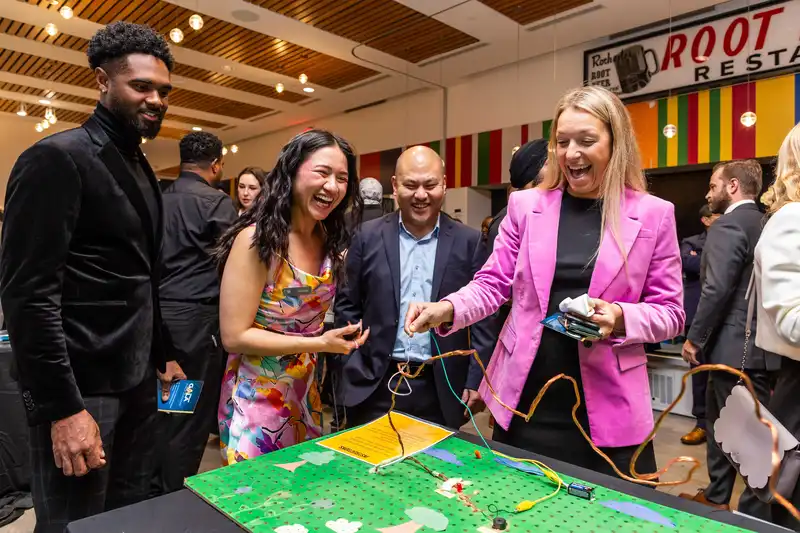 Four people laugh and play an interactive table game at a lively indoor event or party.