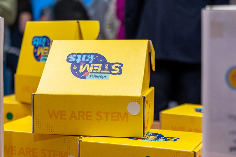 Yellow STEM-themed boxes with WE ARE STEM printed on them, stacked on a table at an event.
