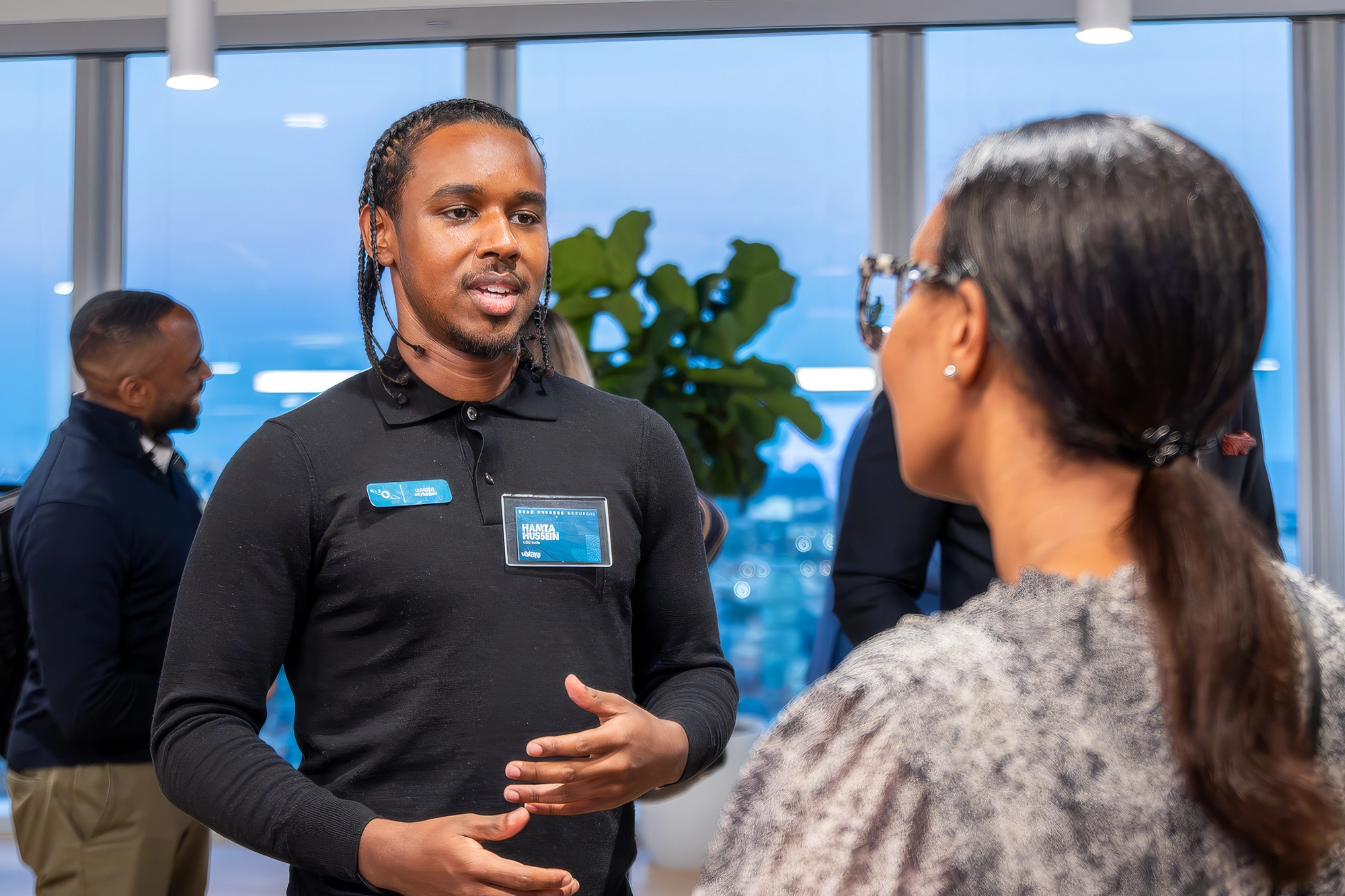 A man with braids speaks to a woman at a professional networking event in a bright office space.