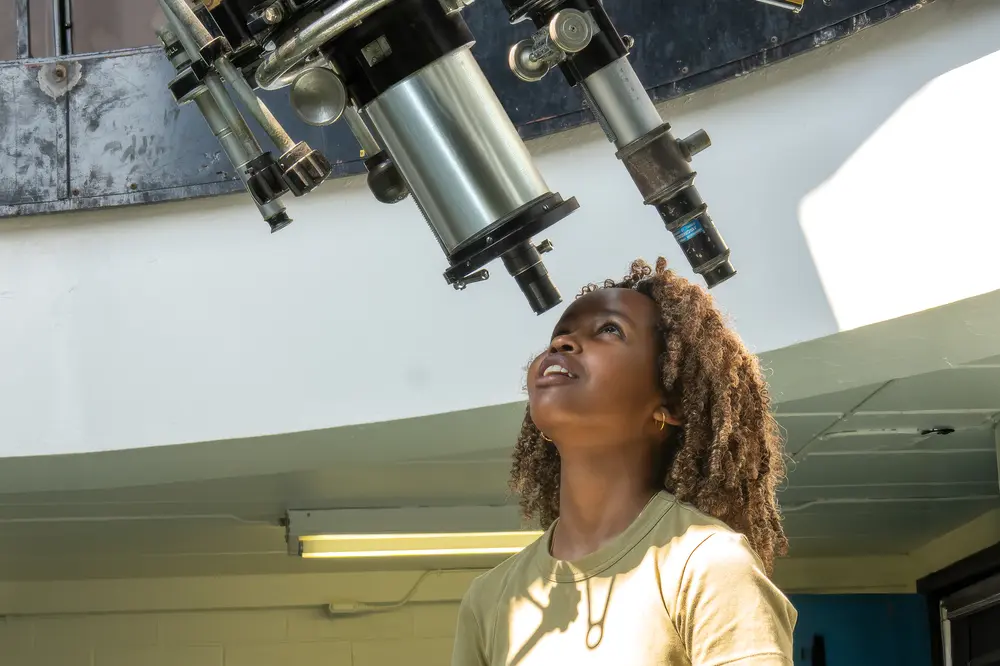 A woman looks up at a large telescope inside an observatory.