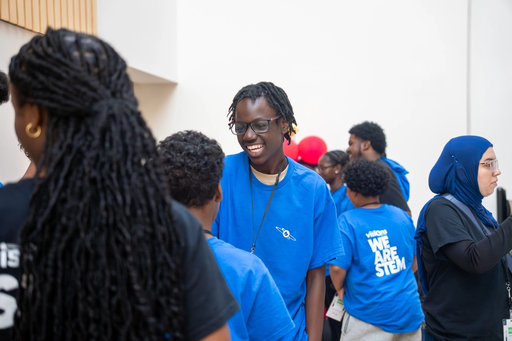 People in blue and black STEM shirts are gathered indoors, talking and smiling at an event.