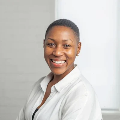 Smiling person with short hair wearing a white shirt, posing in front of a light background.
