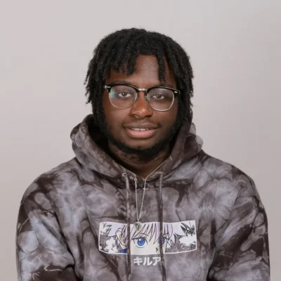 A person with glasses and dreadlocks wearing a tie-dye hoodie with an anime design on the front.