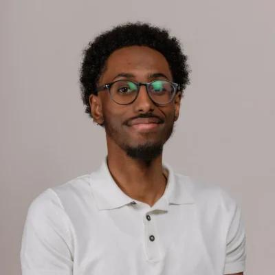 Man with short curly hair, glasses, and a goatee, wearing a white polo shirt and smiling at the camera.
