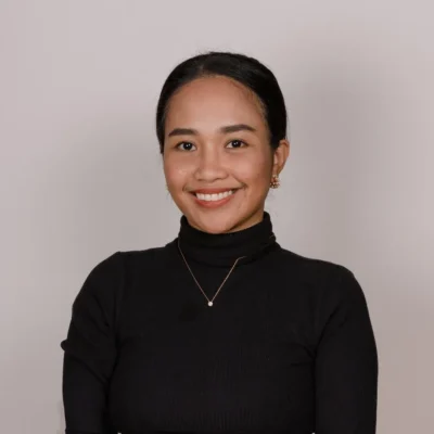Woman with dark hair in a bun, wearing a black turtleneck and gold necklace, smiling at the camera.