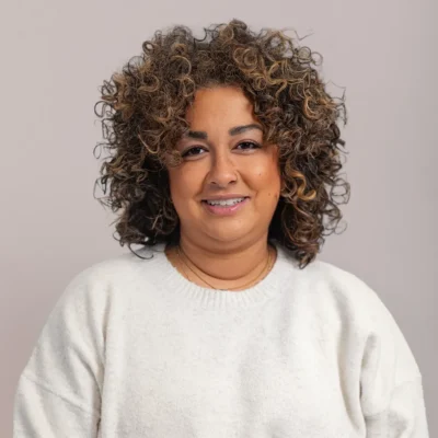 Smiling person with curly hair wearing a white sweater against a plain light background.