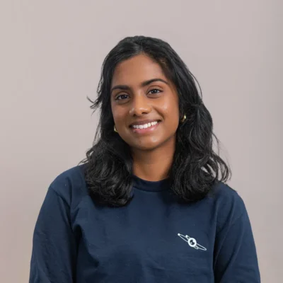 Woman with dark hair smiles, wearing a navy shirt with a small white graphic, on a plain background.