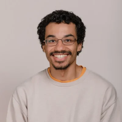 Smiling man with glasses and a beard, wearing a light sweatshirt, poses in front of a neutral background.