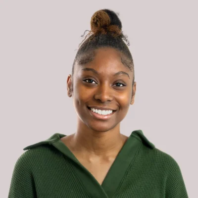 Smiling woman wearing a green sweater with hair in a high bun, posing against a light gray background.