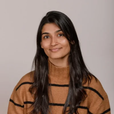 Woman with long dark hair wearing a brown sweater with black stripes, smiling at the camera.