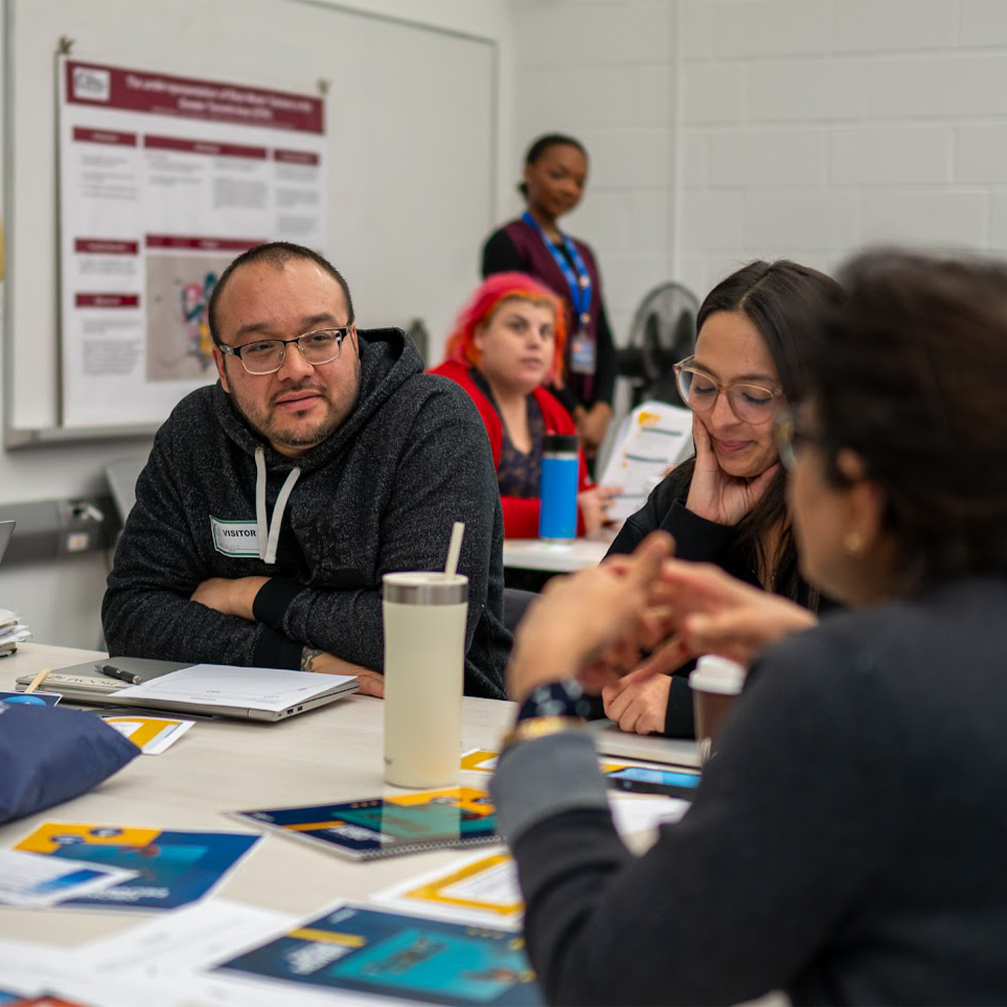 Four people sit around a table in discussion at a classroom workshop, with papers and laptops in front of them.
